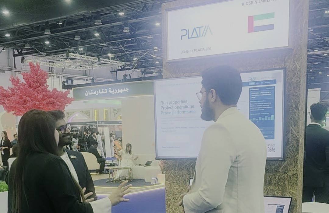 The Platia 360 stand at a UAE industry exhibition, with the EPMS dashboard on screen behind the team